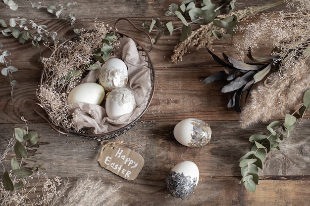 Huevos de Pascua en una canasta decorativa con flores secas sobre una mesa de madera. Concepto de Pascua feliz.