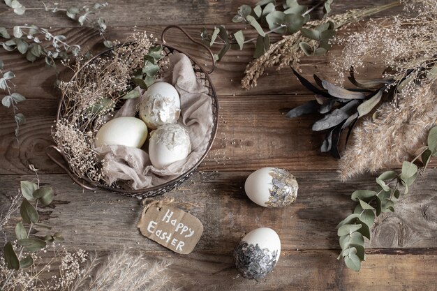 Huevos de Pascua en una canasta decorativa con flores secas sobre una mesa de madera. Concepto de Pascua feliz.