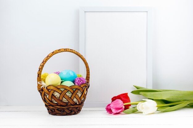 Huevos de Pascua en canasta con tulipanes y marco en blanco