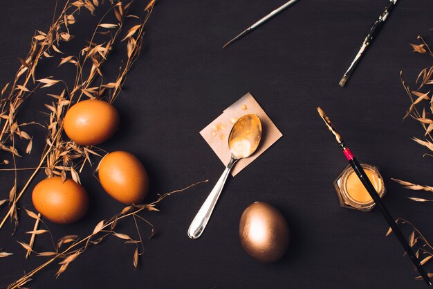 Huevos de pascua cerca de una cuchara sobre papel y pincel sobre tinte entre plantas