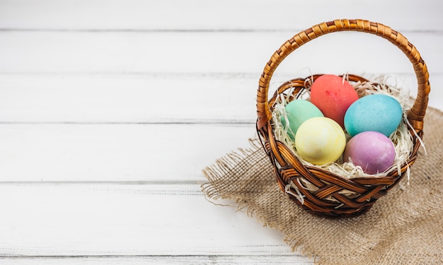 Huevos de Pascua en cesta en mesa de madera