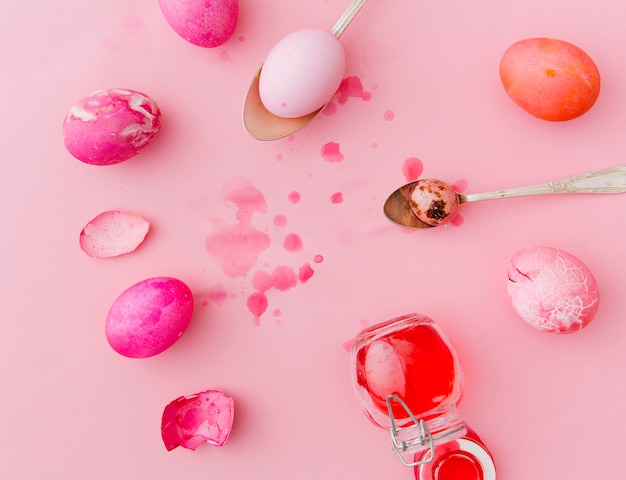 Foto gratuita huevos de pascua color de rosa y rojo cerca de cucharas y latas con tinte líquido