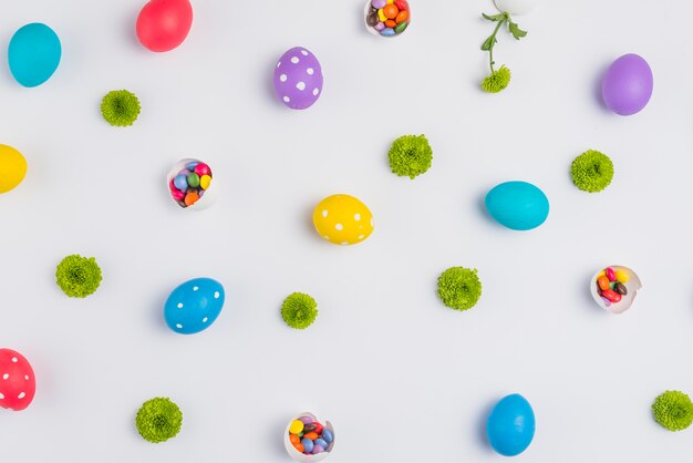 Huevos de Pascua con dulces y flores esparcidas sobre mesa