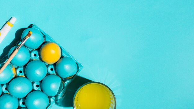 Huevos de Pascua en estante con pincel y vaso de agua en mesa azul