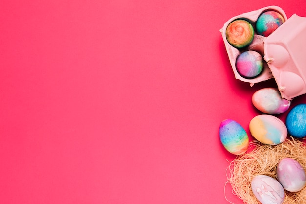 Huevos de Pascua multicolores en caja nido y cartón sobre fondo rosa