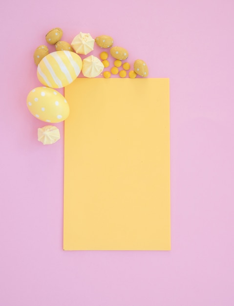 Foto gratuita huevos de pascua con papel amarillo en blanco sobre mesa rosa