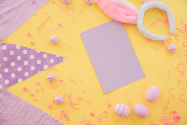 Huevos de Pascua con papel en blanco y orejas de conejo en la mesa