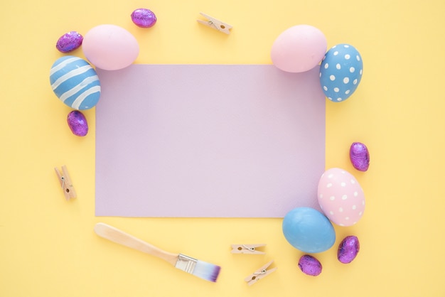 Huevos de Pascua con papel morado en blanco sobre mesa amarilla