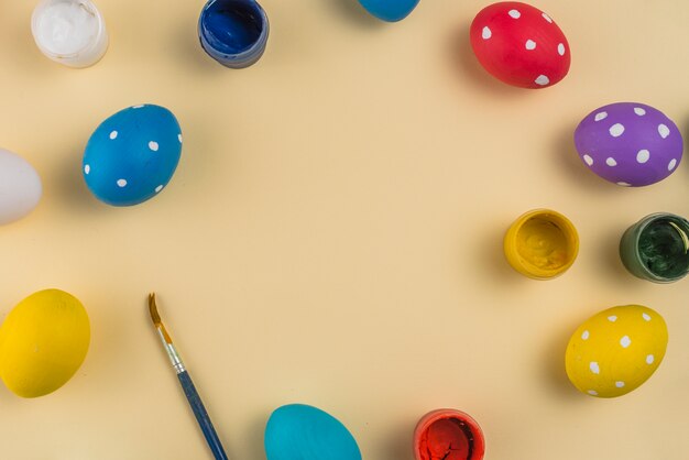 Huevos de Pascua con pinturas y pincel sobre mesa beige