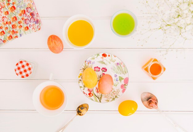 Huevos de Pascua entre la placa cerca de cucharas, servilletas y tazas con líquido tinte