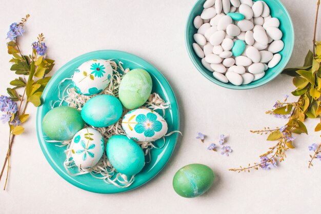 Huevos de Pascua en un plato cerca de pequeñas piedras en ramitas de tazón y flores