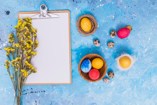 Huevos de Pascua con portapapeles y flores en mesa