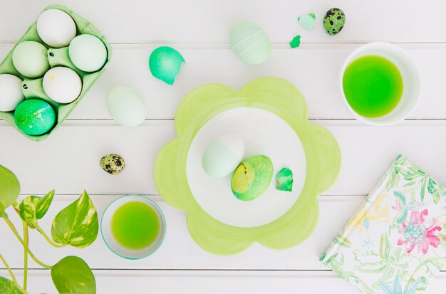 Huevos de Pascua en un recipiente cerca de un plato, servilleta y taza con líquido tinte