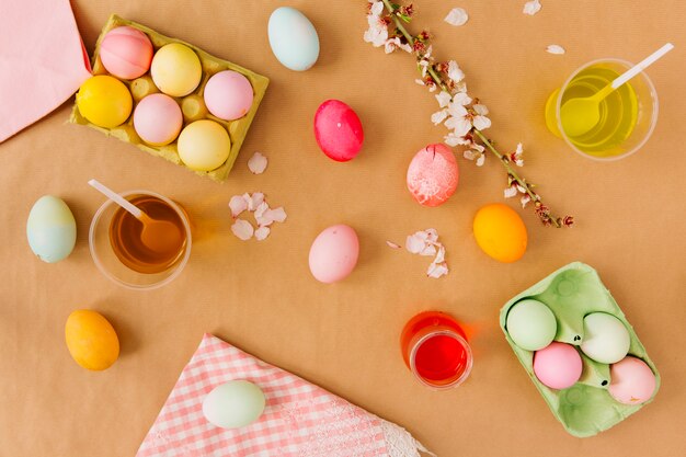 Huevos de Pascua en recipientes cerca de tazas con líquido tinte, servilleta y ramita de flores