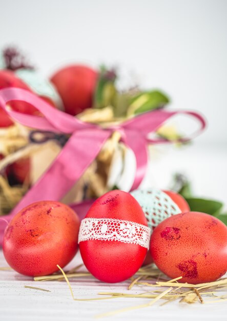 Huevos de Pascua rojos atados con cinta de encaje de cerca, acostado en una canasta de Pascua con un lazo, bodegón