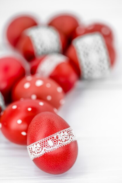 Huevos de Pascua rojos sobre cinta blanca de encaje atado, close-up, acostado sobre una madera blanca