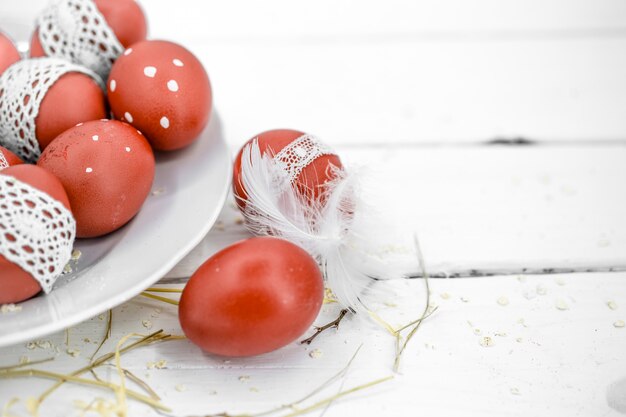 Huevos de Pascua rojos sobre una placa blanca y sobre cinta de encaje atada blanca, close-up