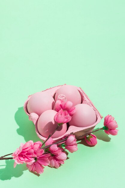 Huevos de Pascua rosados en estante con flores en mesa verde