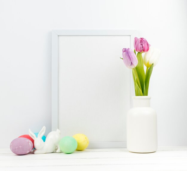 Huevos de Pascua con tulipanes en florero y marco en blanco
