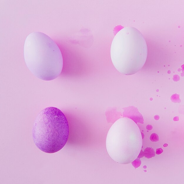 Huevos de Pascua violetas y blancos entre salpicaduras de tinte líquido.