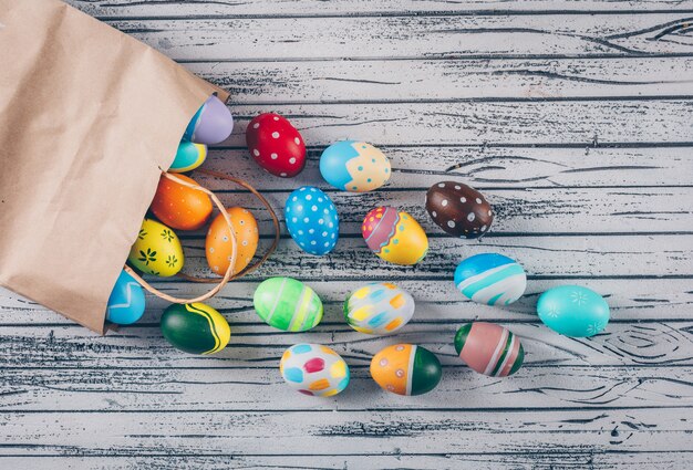 Foto gratuita huevos de pascua de la vista superior que salen de la bolsa de papel sobre fondo de madera claro.