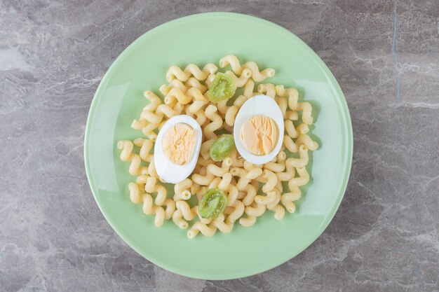 Huevos en rodajas y macarrones en placa verde.