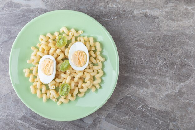 Huevos en rodajas y macarrones en placa verde.