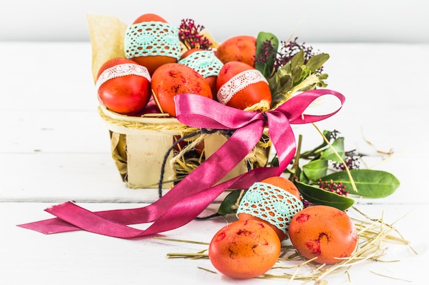 Foto gratuita huevos rojos atados con cinta de encaje, acostado en una canasta de pascua con un lazo