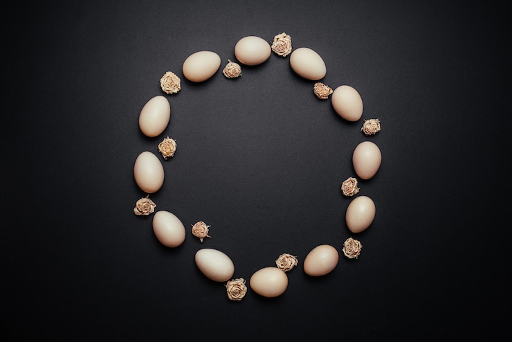Foto gratuito huevos con rosas secas dispuestas en un círculo sobre fondo negro de madera.