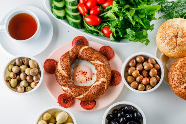 Huevos con salchichas en un plato con una taza de té, panecillos turcos, vista superior de ensalada sobre una superficie blanca