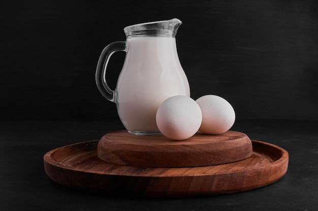 Foto gratuita huevos y un tarro de leche sobre una tabla de madera.