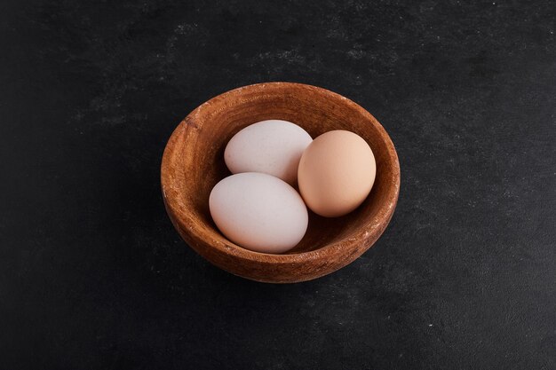 Huevos en una taza de madera en espacio negro.