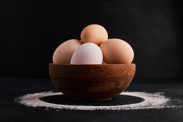 Huevos en una taza de madera en espacio negro.