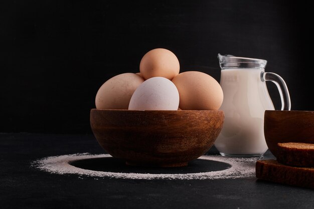 Huevos en una taza de madera con un tarro de leche a un lado.