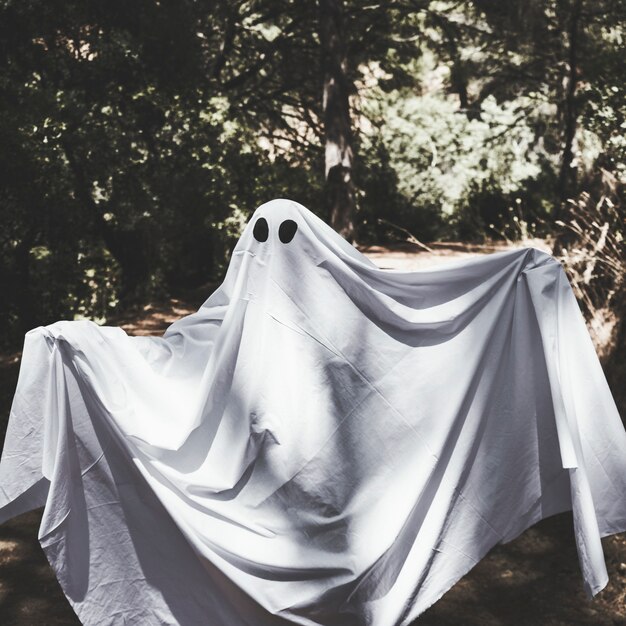 Humano en ropa fantasma con manos en alza en el bosque