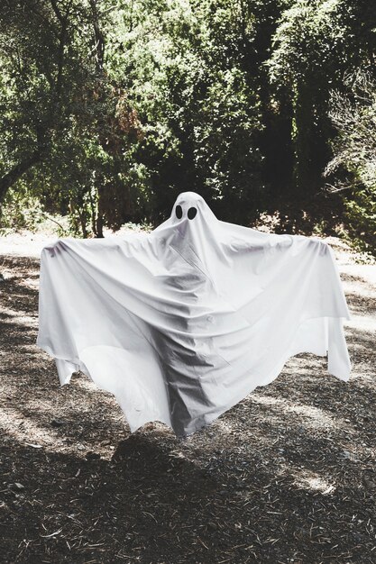 Humano en traje de fantasma con las manos en alza en el bosque