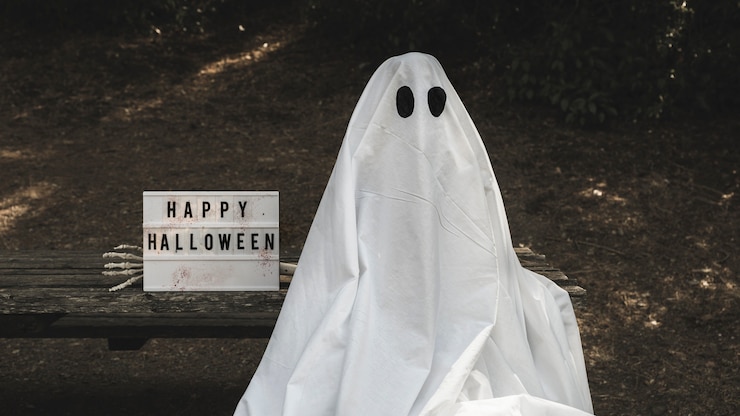 Foto gratuito humano en traje de fantasma sentado en el banco cerca de la tableta de halloween