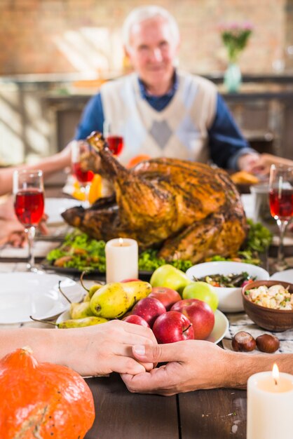 Humanos tomados de la mano en la mesa con comida cerca de hombre envejecido