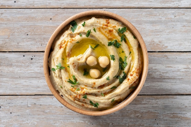 Hummus de garbanzos en un cuenco de madera adornado con pimentón de perejil y aceite de oliva en la mesa de madera