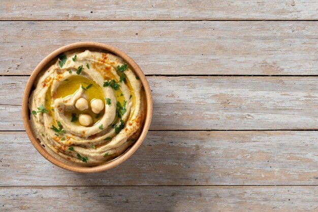 Hummus de garbanzos en un cuenco de madera adornado con pimentón de perejil y aceite de oliva en la mesa de madera