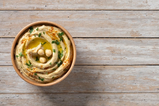 Hummus de garbanzos en un cuenco de madera adornado con pimentón de perejil y aceite de oliva en la mesa de madera