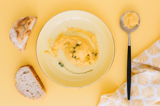 Hummus en un plato y una cuchara con rebanadas de pan sobre fondo beige