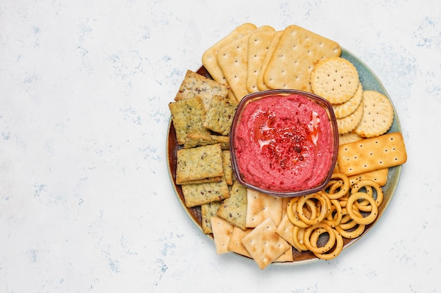 Foto gratuita hummus de remolacha en tabla de cortar con galletas saladas en superficie clara