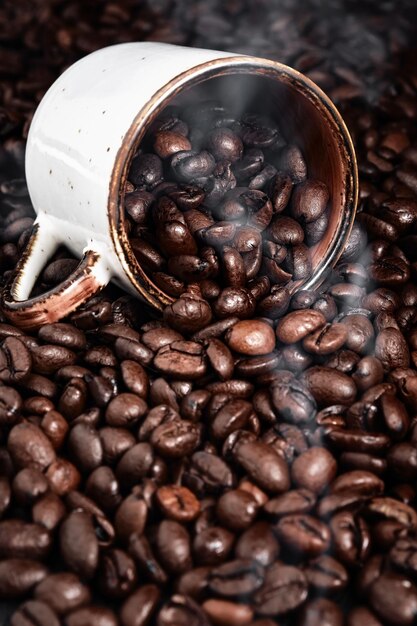 El humo se eleva de los granos de café tostados. La taza de café se encuentra en el enfoque selectivo del café fragante en los frijoles.