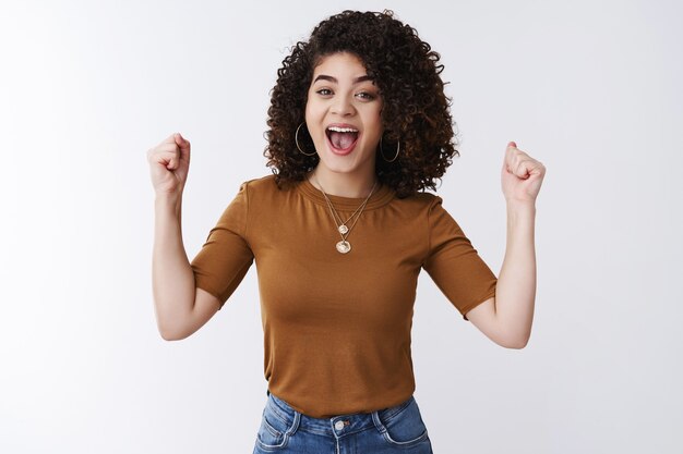 ¡Hurra, buenas noticias! Atractiva chica joven feliz con el pelo rizado oscuro animando apoyo amigo apriete los dedos índices levantados gesto de victoria celebrando felicitando amigo sonriendo con alegría