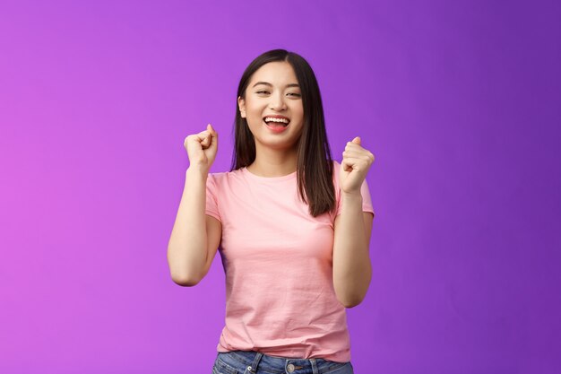 ¡Hurra victoria afortunada! La chica asiática atractiva alegre hace la bomba de puño, el baile celebra la victoria, se para el fondo púrpura alegre, logra excelentes noticias sonriendo alegremente, mueve la música rítmica.