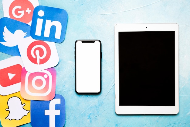 Iconos de redes sociales con teléfono celular y tableta digital en pared pintada de azul