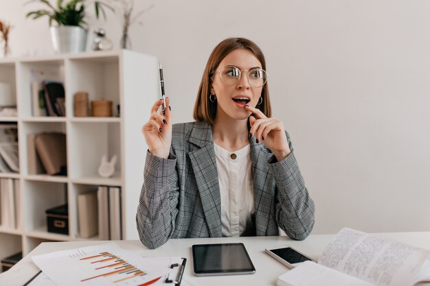 Una idea brillante vino a la mente de una joven mujer de negocios con elegante chaqueta y gafas sentada en el lugar de trabajo.