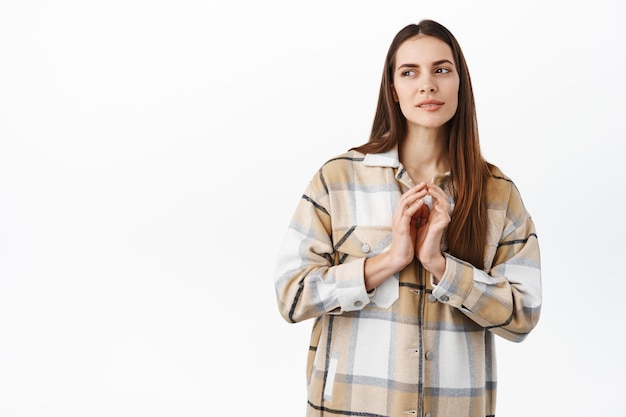 Idea interesante. Plan intrigante de mujer joven pensativa, dedos de campanario y mirando a un lado con mirada pensativa y decidida, de pie tortuoso contra el fondo blanco