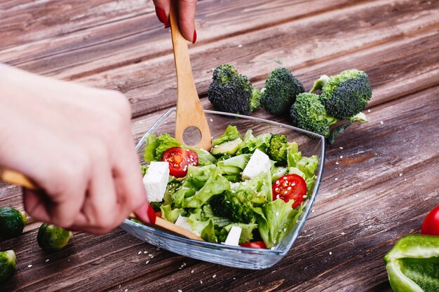 Ideas para el almuerzo o la cena. Mujer agita ensalada fresca de verdor, aguacate, pimiento verde.